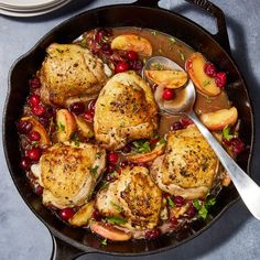 a skillet filled with chicken and cranberries on top of a blue table