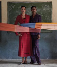 a man and woman standing in front of a blackboard with colorful strips on it