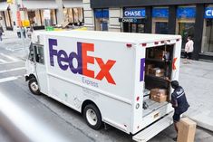 a fed ex truck is parked on the side of the street as people walk by