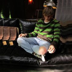 a young man sitting on top of a black leather couch in front of a lamp