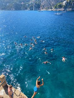 people swimming in the blue water near some cliffs and mountains, while others swim nearby