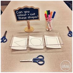 scissors, paper and markers sit on a table with a sign that says can you cut these shapes?