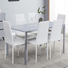 a dining room table with white chairs and a vase on the floor next to it