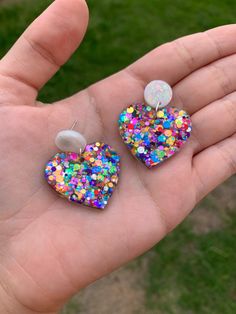 a hand holding two heart shaped earrings with colorful sprinkles and pearls on them