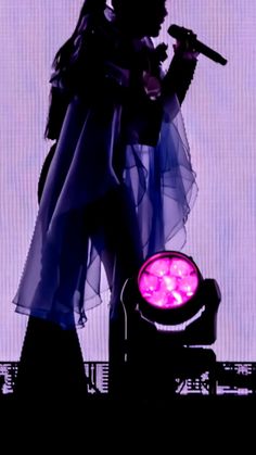 the silhouette of a woman holding a microphone in front of a purple light on stage