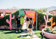 three people standing in front of a cactus garden with pink and green signs that say desert style