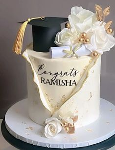 a graduation cake decorated with white flowers and black mortar on top, topped with a gold tassel