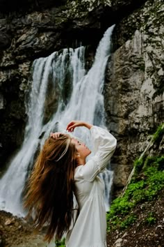 a woman with long hair standing in front of a waterfall