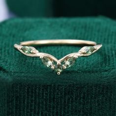 a gold ring with three green stones on it's side, sitting on top of a green velvet box