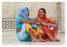 two women sitting on the ground talking to each other in front of a white wall