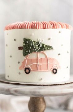 a cake decorated with pink icing and a car carrying a christmas tree on top