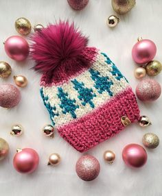 a knitted hat with pink and blue pom - poms surrounded by christmas ornaments