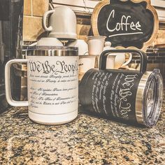 two coffee mugs sitting on top of a counter next to a chalkboard sign