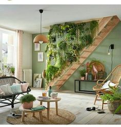 a living room filled with lots of plants on the wall next to a stair case