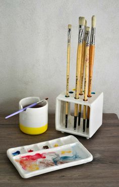 the paintbrushes are sitting on the tray next to the cup and brush holder