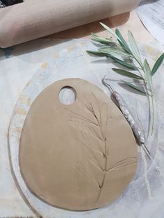 a piece of clay sitting on top of a table next to a rolling pin and some leaves