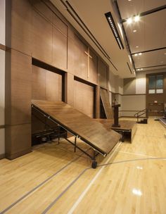 an empty gym with hard wood flooring and wooden stairs leading up to the upper level