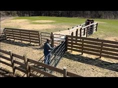 a man standing in front of a fence next to a sheep pen on top of a grass covered field