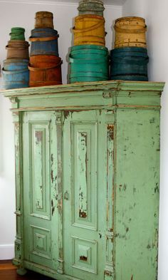 an old green cabinet with many different colored pots on it's top and bottom