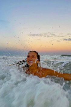 a woman smiles as she rides the waves on her surfboard in the ocean at sunset