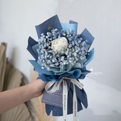 a person holding a bouquet of blue and white flowers in their hand with the tag on it