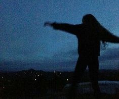 a woman standing on top of a hill at night with her arms spread out in the air