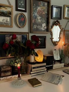 a table topped with books and vases filled with red roses next to a mirror