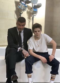 a man sitting next to a young boy on top of a white bench in front of a camera