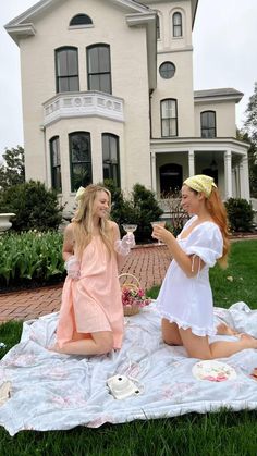 two beautiful women sitting on top of a blanket in front of a large white house