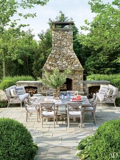 an outdoor dining table with chairs around it and a fire place in the back ground