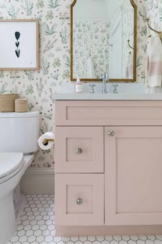 a bathroom with pink cabinets and floral wallpaper on the walls, along with a gold framed mirror