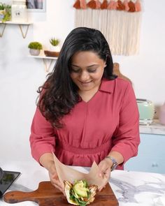 a woman in a pink shirt is cutting up a sandwich on a wooden board with a knife