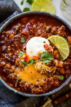 a bowl filled with chili and sour cream on top of a wooden table next to limes