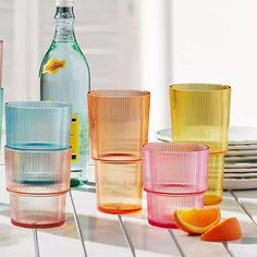 there are many different colored glasses next to each other on the table with plates and bottles in the background