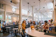 people sitting at tables in a restaurant with lots of lights hanging from the ceiling and windows