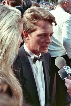 a man in a suit and bow tie talking to someone on the red carpet at an event