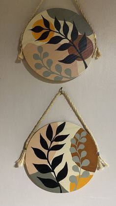 two circular wooden hangings with plants painted on them, one has a rope and the other is decorated with leaves