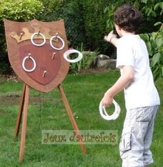 a young boy standing in front of a wooden sign with rings on it's face