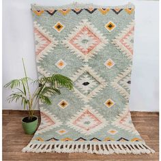 a green and orange rug sitting on top of a wooden floor next to a potted plant