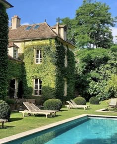 an outdoor swimming pool surrounded by lush green plants and lawn furniture next to a large house