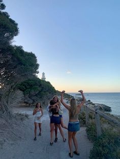 three girls standing on a path near the ocean with their arms up in the air