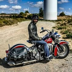 a man is sitting on his motorcycle in front of a wind tower and dirt road