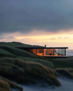 a house sitting on top of a lush green hillside next to the ocean at sunset