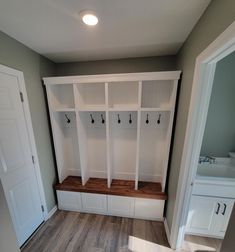 an empty room with white cabinets and wooden bench in the center, on top of hard wood flooring