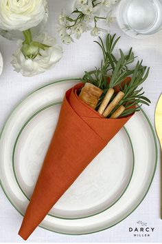 a carrot shaped napkin holder on top of a white plate next to flowers and utensils