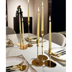 a white table topped with gold place settings and tall candlesticks on top of it