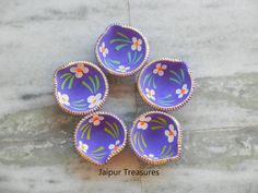 four purple bowls with flowers painted on them sitting on a tile floor next to a wall