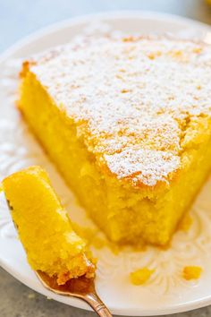 a slice of lemon cake on a white plate with a gold spoon and some powdered sugar