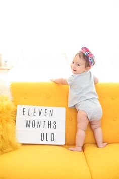 a baby sitting on top of a yellow couch next to a sign that says eleven months old