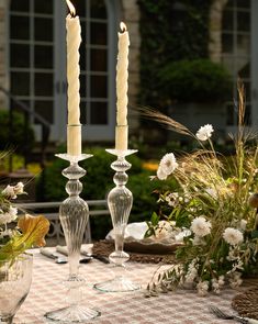 two tall candles are sitting on a table with flowers and greenery in the background